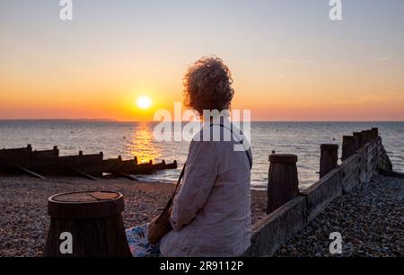 Whitstable North Kent , Inghilterra Regno Unito - Una donna gode del tramonto sull'estuario del Tamigi Foto Stock