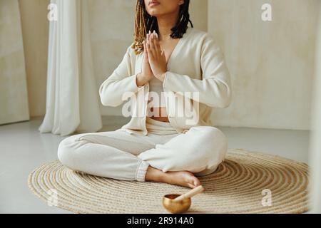 Immagine ritagliata di una donna africana seduta sul pavimento a casa e che si tiene per mano in mudra mentre meditava. Foto Stock