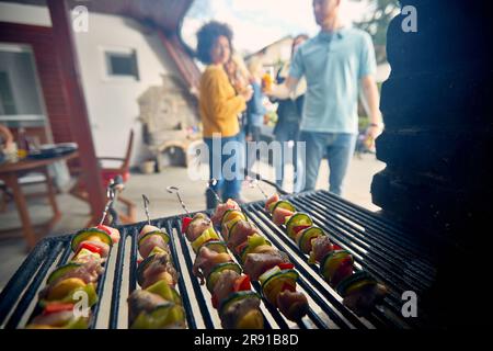 Vista ravvicinata di un grill frizzante. Le griglie per grigliate offrono piatti perfettamente cotti. Sullo sfondo, è possibile vedere un gruppo di persone riunite intorno. Foto Stock