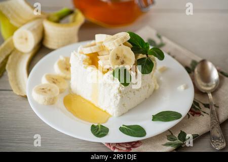 Porzione di cagliata di latte fatta in casa con fette di banana e miele, con menta in un piatto. Foto Stock