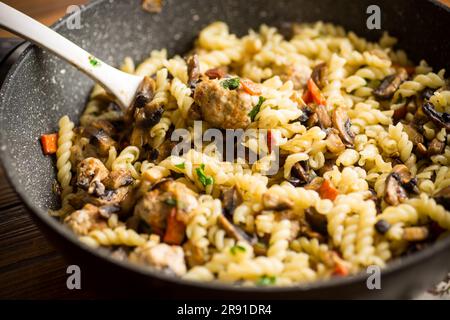 vermicelli cotti con funghi, carne e verdure in padella su un tavolo di legno Foto Stock