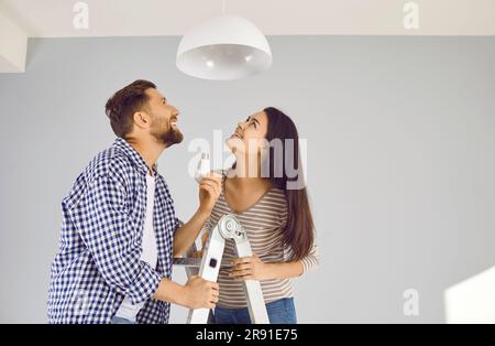 Felice giovane coppia di famiglia che cambia una lampadina nella lampada da soffitto di casa loro Foto Stock