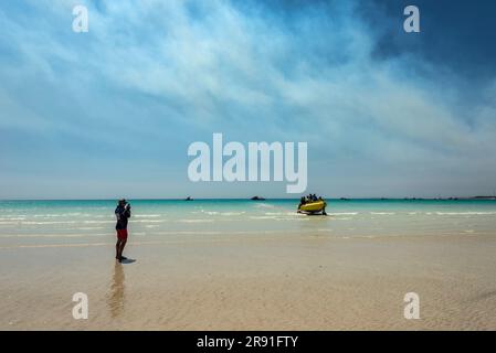 Una persona scatta una foto di una barca su ruote che emerge dall'acqua sulla Cable Beach a Broome, Australia Occidentale Foto Stock