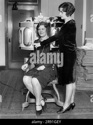 New York, New York: c. 1930 Una donna pioniera sta per somministrare un trattamento del nuovo processo fotoletico Frigidine di peeling cutaneo a un cliente. Viene somministrato 20 minuti al giorno per 5 giorni, quando sei ore dopo l'ultimo trattamento la vecchia pelle macchiata si stacca rivelando una nuova pelle priva di difetti, lentiggini e linee. Foto Stock
