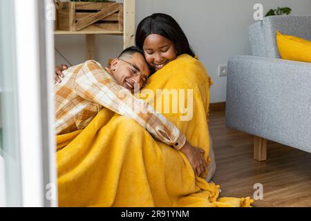 Uomo che abbraccia una donna coperta di scialle giallo a casa Foto Stock
