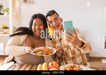 Coppia felice che si prende un selfie con il cibo al tavolo da pranzo Foto Stock