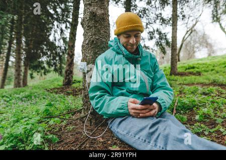 Uomo che utilizza la ricarica dello smartphone con presa sul tronco Foto Stock