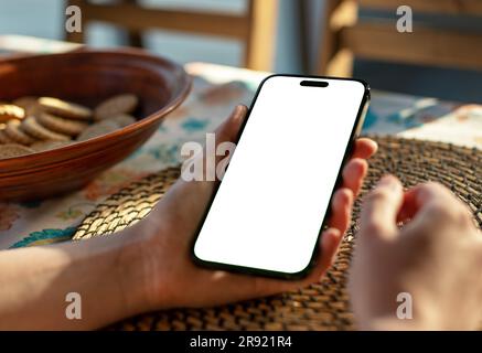 Lodz, Polonia 19 giugno 2023 mockup dello schermo del telefono cellulare tenuto a mano al tavolo della cena. Foto Stock
