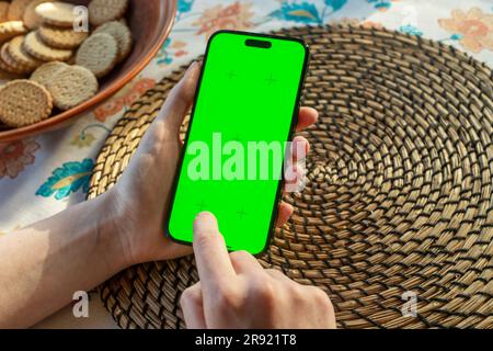 Lodz, Polonia 19 giugno 2023 mano utilizzando lo schermo dello smartphone mockup al tavolo della cena. Foto Stock