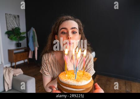 Giovane donna che soffia candele sulla torta di compleanno a casa Foto Stock