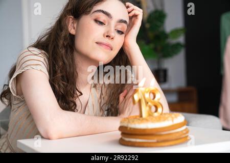 Una giovane donna premurosa davanti alla torta di compleanno a casa Foto Stock