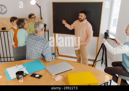 Uomo in piedi di fronte alla lavagna che tiene una lezione in linea Foto Stock