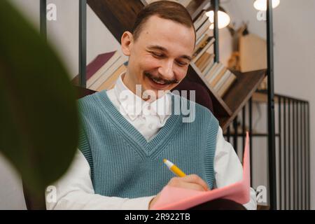 Uomo sorridente con baffi che prende appunti seduto in studio Foto Stock