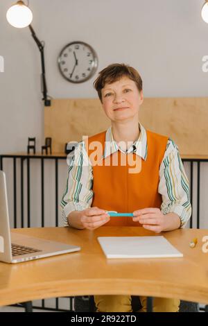 Donna sorridente seduta in classe che guarda una videocamera che registra una lezione online Foto Stock