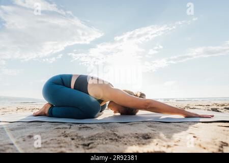 Donna matura che pratica la posa yoga con il cielo sullo sfondo in spiaggia Foto Stock