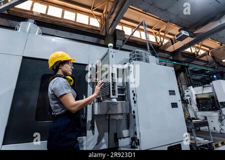Tecnico addetto alla manutenzione che indossa elmetto utilizzando la tastiera della macchina CNC in fabbrica moderna Foto Stock
