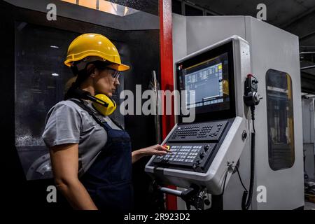Ingegnere che indossa la tastiera per macchine CNC a elmetto in fabbrica moderna Foto Stock