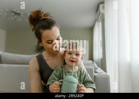 Madre seduta con una figlia che tiene a casa il biberon Foto Stock