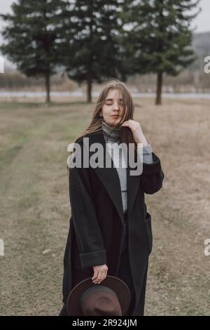 Giovane donna che indossa un lungo cappotto in piedi sul campo Foto Stock