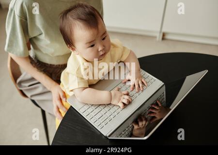 Simpatica figlia che digita sul laptop seduta con la madre a casa Foto Stock
