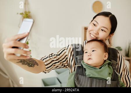 Donna sorridente che prende selfie con la figlia attraverso lo smartphone a casa Foto Stock