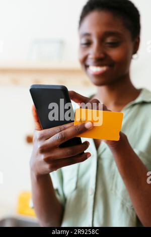 Donna sorridente che effettua il pagamento tramite carta di credito sul cellulare a casa Foto Stock