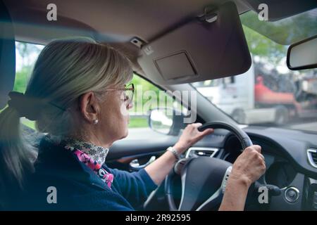 Donna anziana che indossa occhiali da vista che guida un'auto Foto Stock