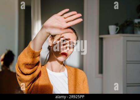 Donna che protegge gli occhi dalla luce del sole a casa Foto Stock