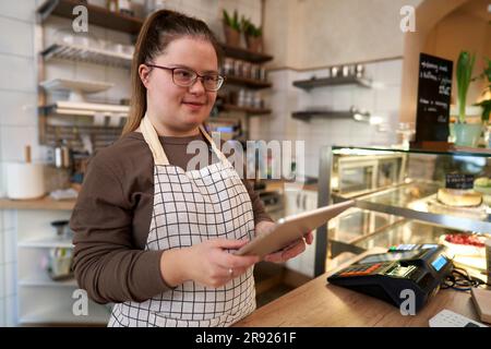 Proprietario di un bar sorridente con sindrome di Down in piedi con un tablet PC Foto Stock