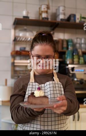 Proprietario di un caffè sorridente con sindrome di Down che dà una fetta di torta Foto Stock