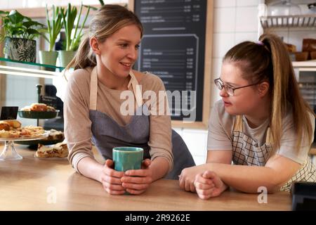 Proprietario di un caffè sorridente con sindrome di Down che parla con un collega Foto Stock