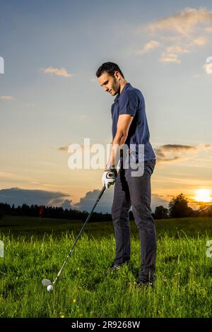 Giovane che si prepara a giocare a golf su erba al crepuscolo Foto Stock