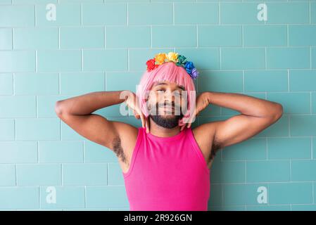 Sorridente queer con fiori sulla testa davanti a una parete piastrellata Foto Stock