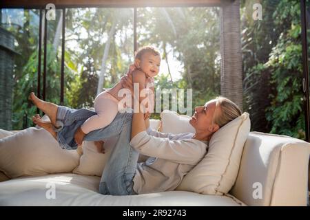 Mamma felice che gioca con la figlia sul divano in salotto Foto Stock