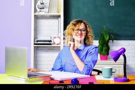 Giornata mondiale degli insegnanti. Insegnante professionista o professore universitario in classe. Giovane insegnante in occhiali nella classe scolastica. Studentessa seduta al tavolo Foto Stock