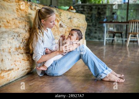 Madre con figlia seduta sul pavimento in cucina a casa Foto Stock