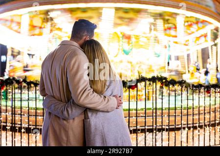 Coppia che si abbracciano davanti al carosello al mercatino di Natale Foto Stock