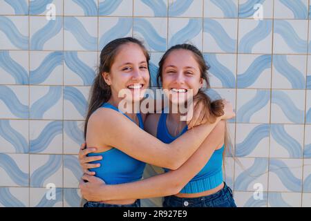 Sorelle gemelle che si abbracciano davanti al muro Foto Stock