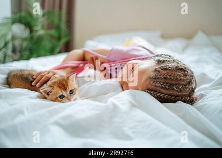 Ragazza che gioca con ginger gitten sul letto Foto Stock