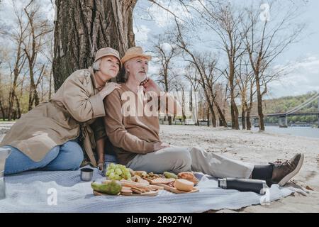 Coppia seduta su una coperta da picnic con spuntini in spiaggia Foto Stock