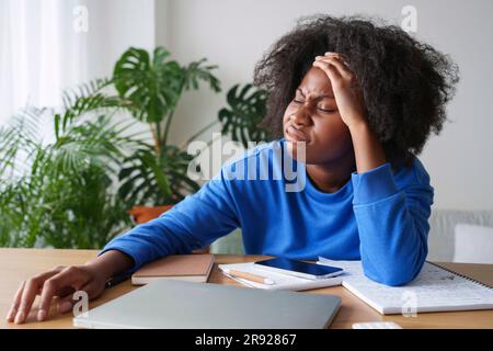 Frustrata donna d'affari afro con la testa in mano alla scrivania Foto Stock