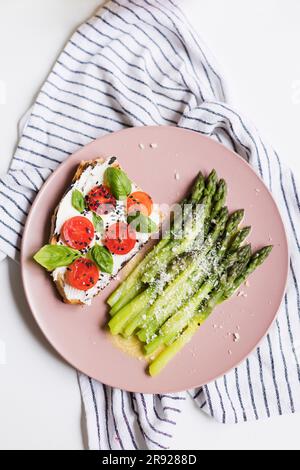 Colazione salutare con asparagi verdi e sandwich a pasta madre con pomodori freschi, foglie di basilico e semi di sesamo Foto Stock