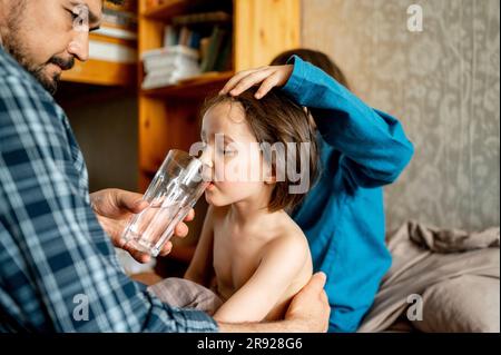 Padre che dà acqua al figlio malato a casa Foto Stock