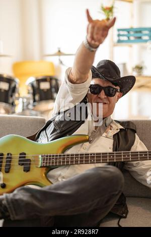 Felice chitarrista che indossa cappello e un cartello con il corno a casa Foto Stock