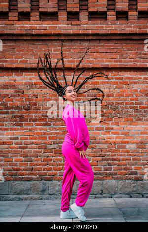 Donna sorridente con dreadlocks in piedi davanti al muro di mattoni Foto Stock