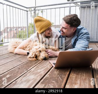 Coppia felice che si trovava sul pavimento con un computer portatile e un cane Foto Stock