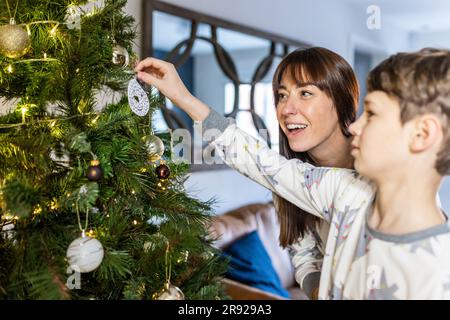Madre e figlio felici che decorano l'albero di Natale a casa Foto Stock