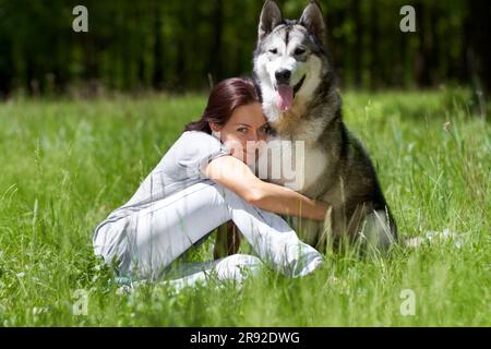 Donna, husky e sorriso in ritratto, campo o parco con abbraccio, amore e legame con cura al sole d'estate. Ragazza, cane da compagnia e felice nella natura, nel bosco o.. Foto Stock