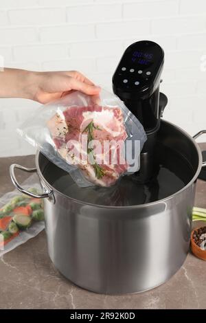 Donna che mette la carne sottovuoto impaccata in pentola con cucina sous vide, primo piano. Circolatore a immersione termica Foto Stock