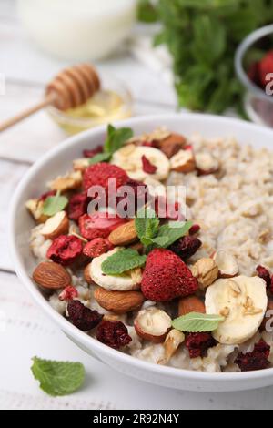 Deliziosa farinata d'avena con frutti di bosco liofilizzati, banana, noci e menta su tavolo bianco, primo piano Foto Stock